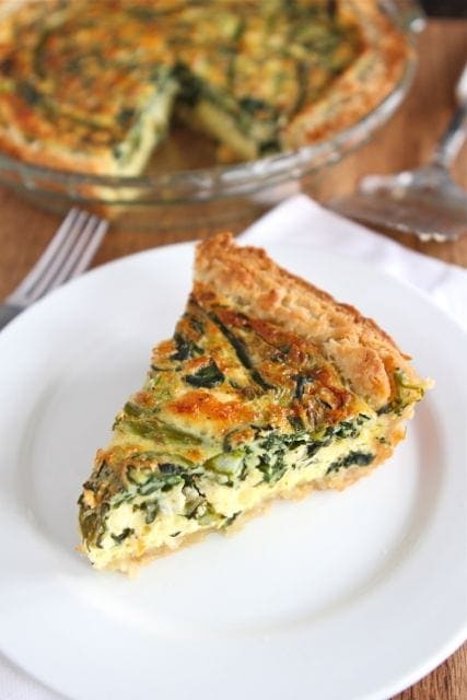 A slice of Asparagus Quiche with visible asparagus spears, colorful bell peppers, and crumbled feta cheese.