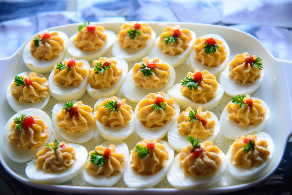 Deviled eggs decorated as sailboats with colorful vegetable sails and paprika sprinkling.