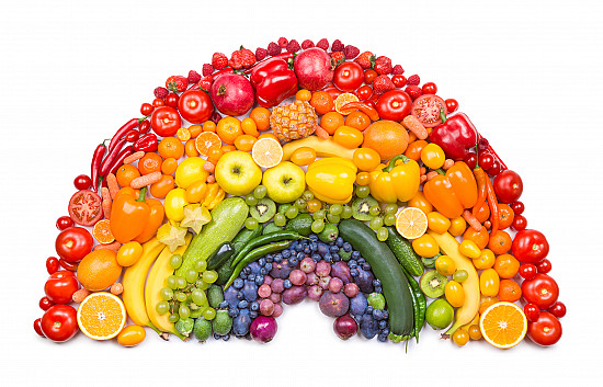 An array of brightly colored fruits and vegetables arranged in a rainbow pattern on a wooden table.
